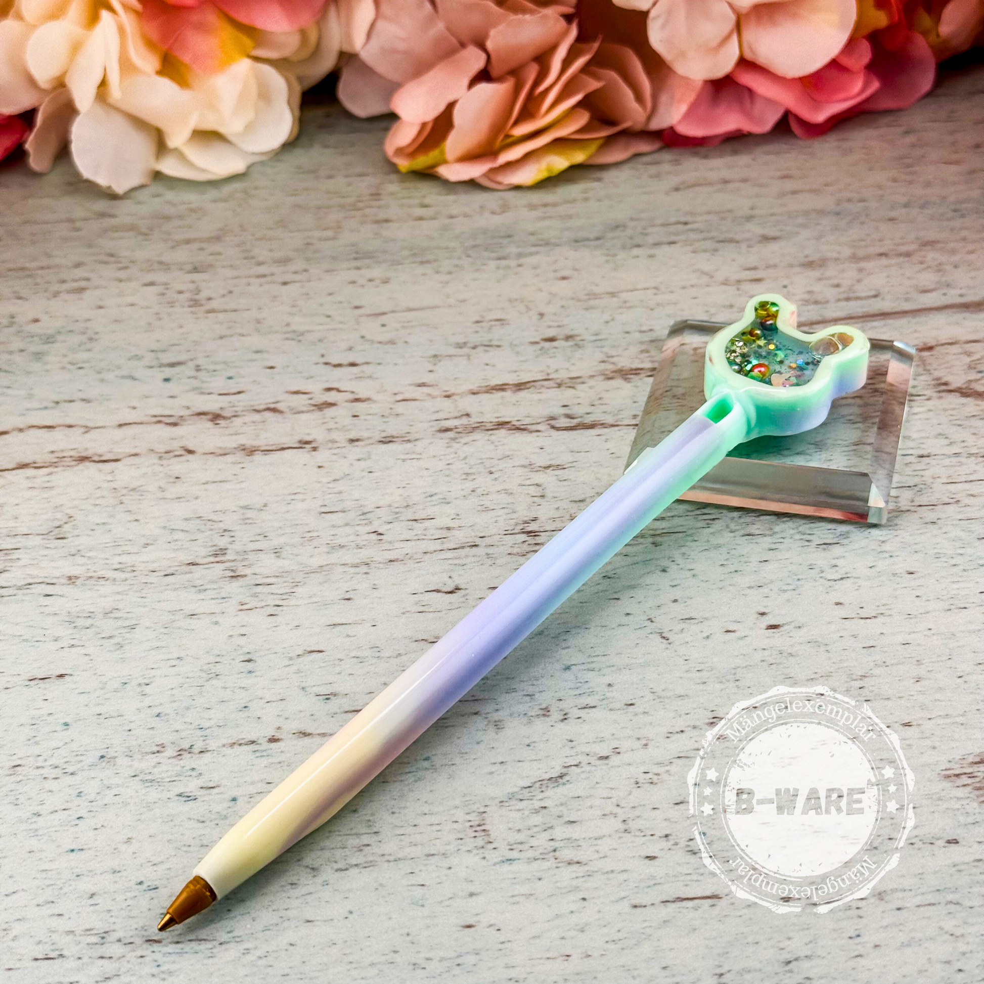Resin-Stift mit Regenbogen-Farbverlauf und Hasenkopf-Shaker, mit gut sichtbarem B-Ware-Stempel im unteren Bereich