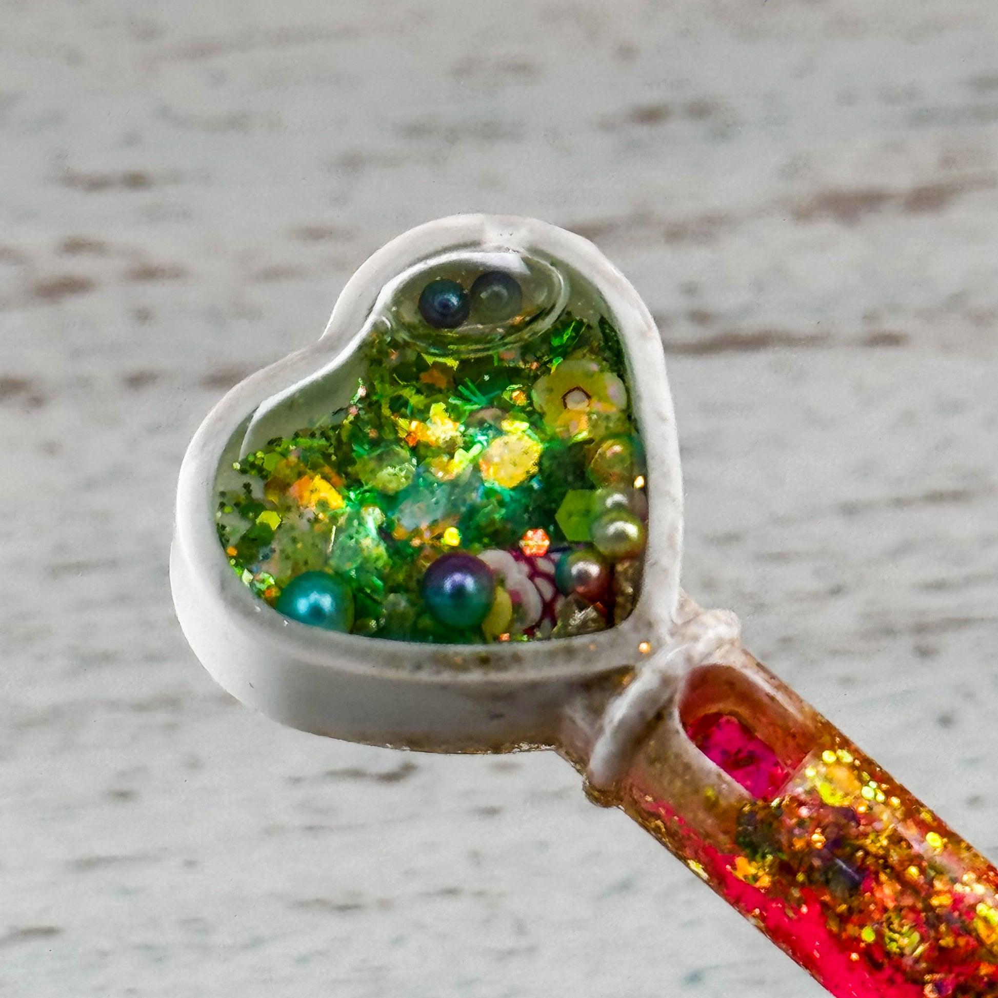 Nahaufnahme des Herz-Shaker-Aufsatzes mit Perlen, Glitzer und Schimmerpartikeln in grün-gold